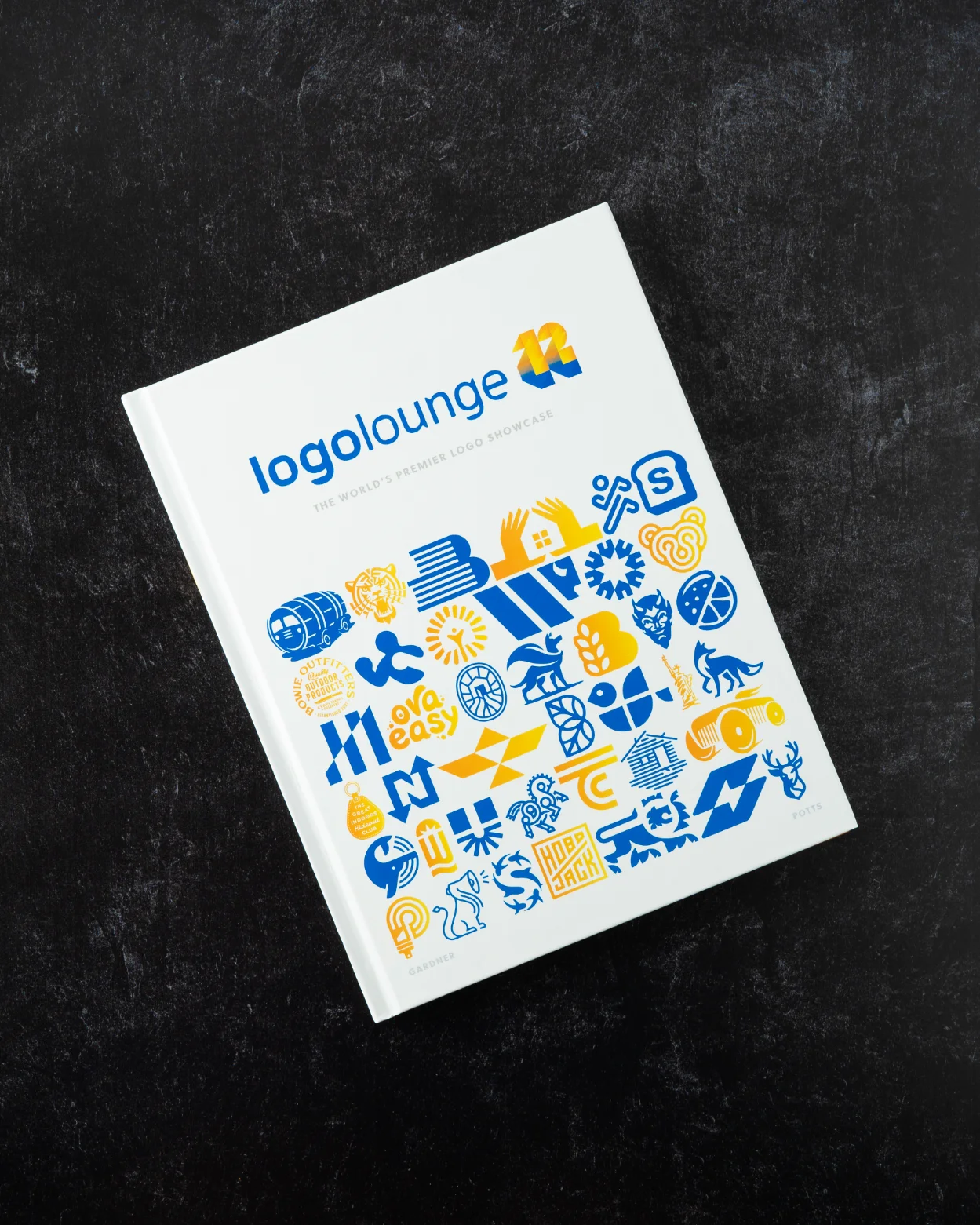 Cover of the LogoLounge 12 book displayed against a dark slate replica surface - zeropoint7 Studio